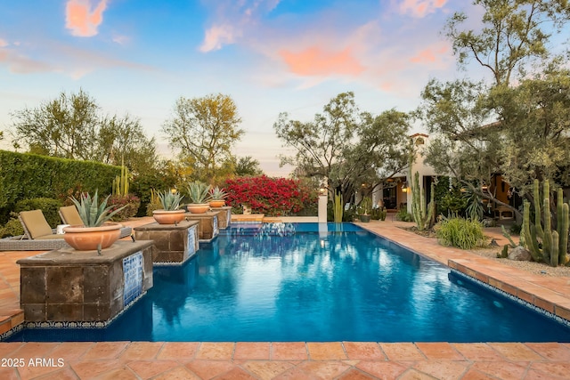 pool at dusk featuring an outdoor pool and a patio