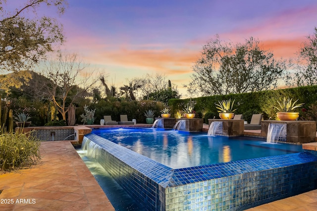 pool at dusk featuring an infinity pool and a patio area