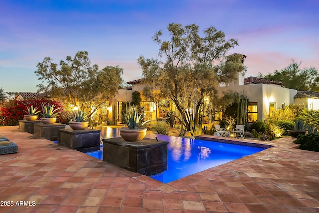 pool at dusk featuring an outdoor pool and a patio