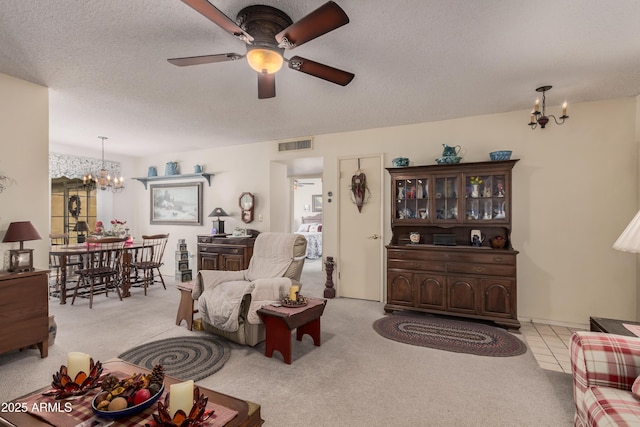 living room with ceiling fan with notable chandelier, a textured ceiling, and light carpet