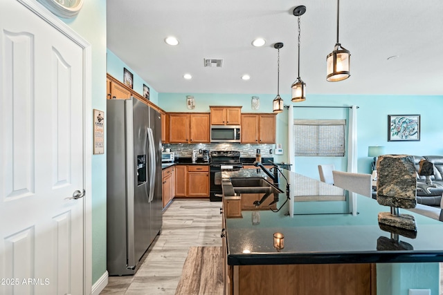 kitchen featuring decorative backsplash, appliances with stainless steel finishes, light wood-type flooring, sink, and decorative light fixtures