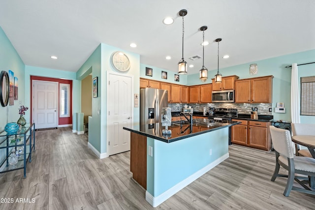 kitchen featuring decorative backsplash, stainless steel appliances, pendant lighting, light hardwood / wood-style floors, and an island with sink