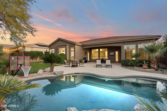 rear view of property with stucco siding, a fire pit, an outdoor pool, and a patio