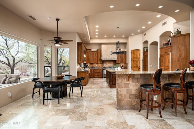 kitchen featuring hanging light fixtures, a large island, light stone counters, decorative backsplash, and high end stove