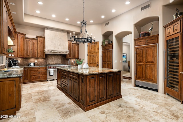 kitchen with hanging light fixtures, range with two ovens, premium range hood, light stone countertops, and a kitchen island