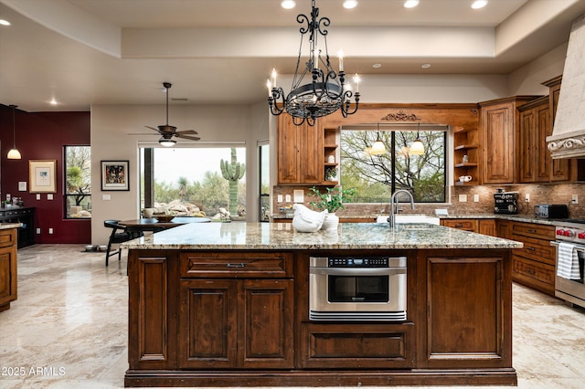 kitchen featuring a raised ceiling, an island with sink, sink, and light stone counters