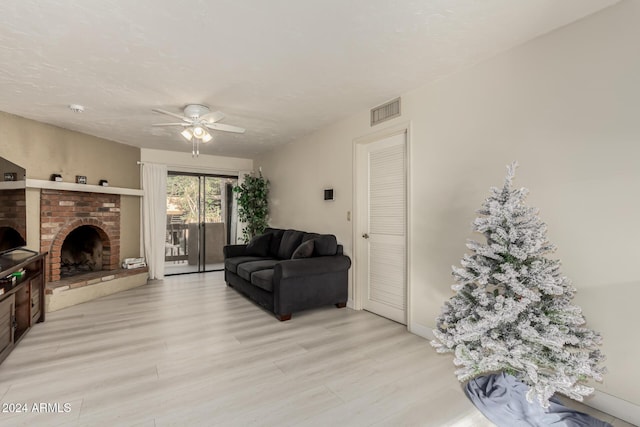 living room with ceiling fan, a brick fireplace, a textured ceiling, and light wood-type flooring