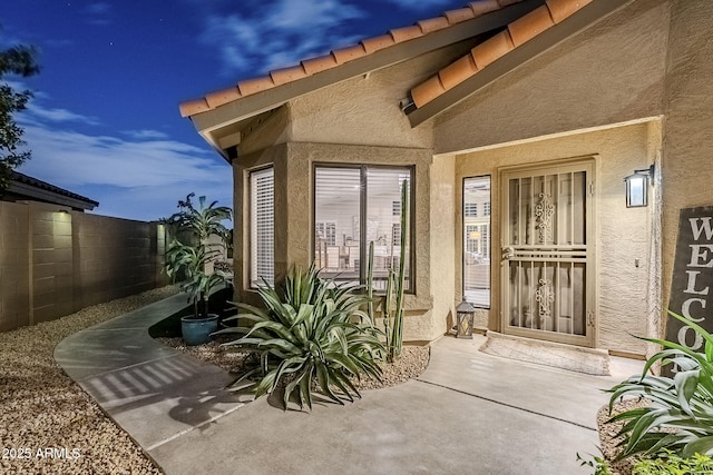 entrance to property featuring a tile roof, fence, and stucco siding