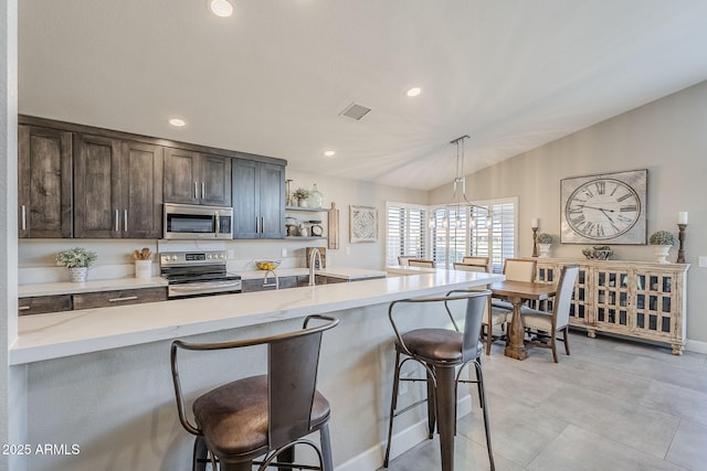 kitchen featuring dark brown cabinetry, lofted ceiling, appliances with stainless steel finishes, a breakfast bar, and open shelves