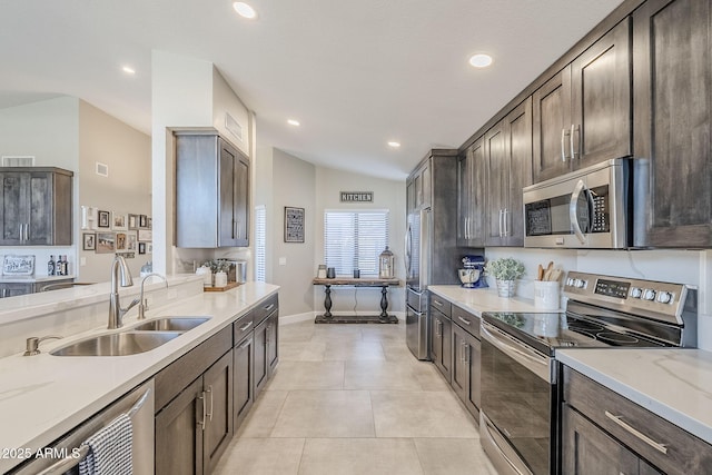 kitchen featuring light tile patterned floors, lofted ceiling, a sink, dark brown cabinets, and appliances with stainless steel finishes