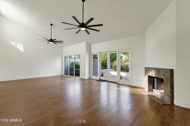 unfurnished living room featuring ceiling fan, a premium fireplace, dark wood-type flooring, and a towering ceiling