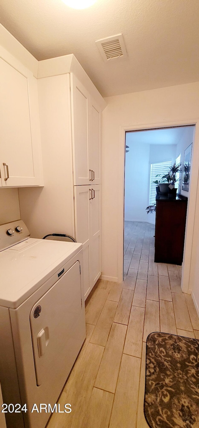 laundry room with washer / dryer, light hardwood / wood-style flooring, and cabinets