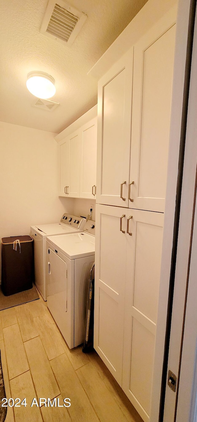 laundry area with washer and dryer, a textured ceiling, and cabinets