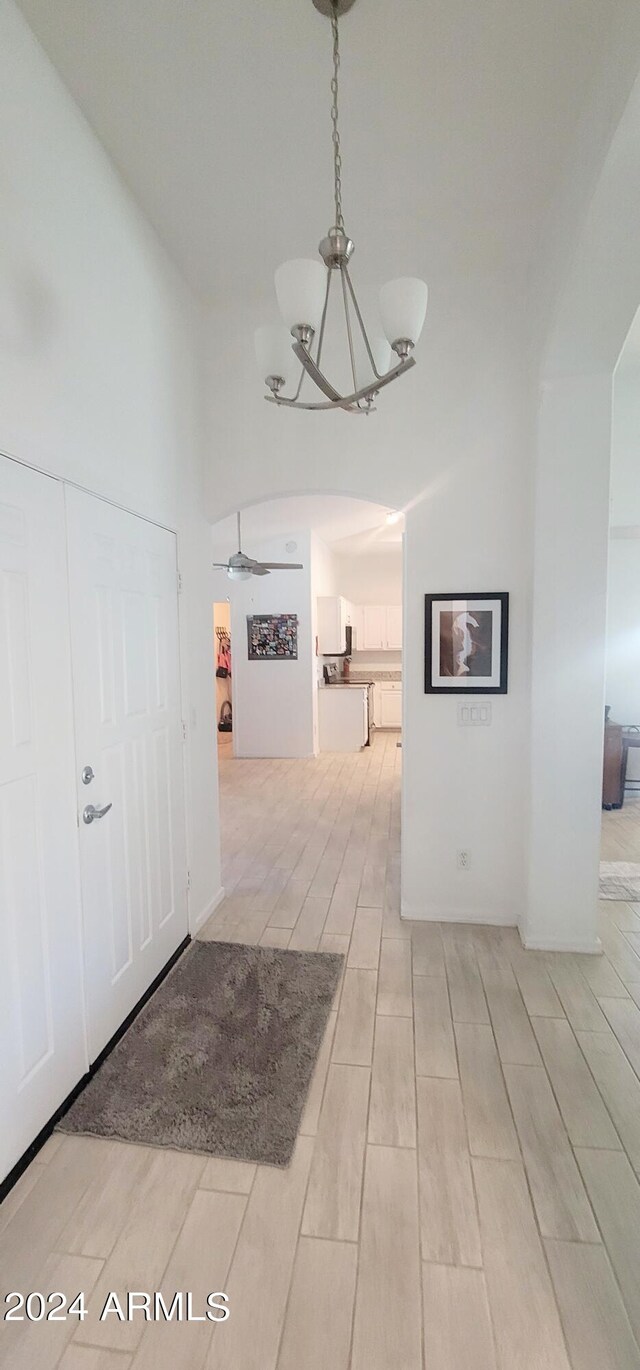 hall with a notable chandelier, a towering ceiling, and light hardwood / wood-style flooring