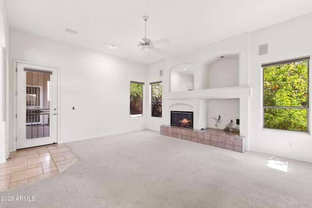 unfurnished living room featuring a tiled fireplace, plenty of natural light, carpet, and a ceiling fan