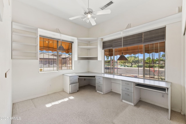 unfurnished office with light carpet, a ceiling fan, built in desk, and visible vents