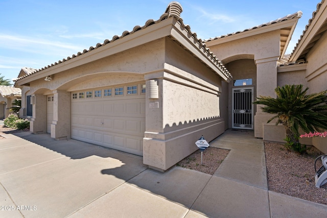 exterior space with concrete driveway, an attached garage, a tile roof, and stucco siding