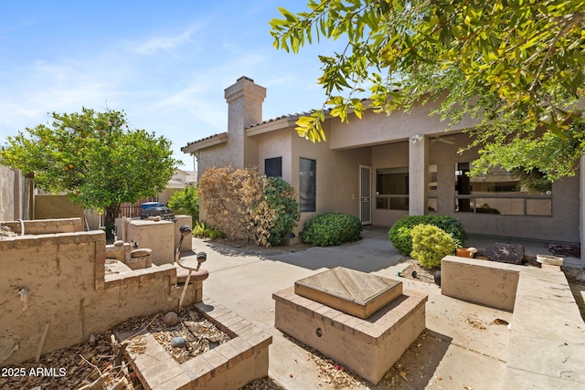rear view of house with a chimney, fence, an outdoor fire pit, a patio, and stucco siding