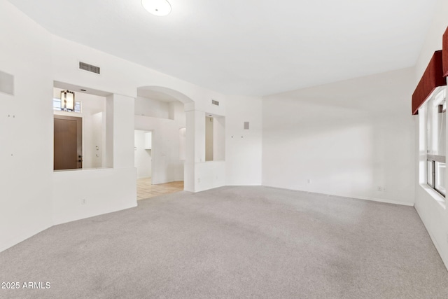 unfurnished room with visible vents, arched walkways, and light colored carpet