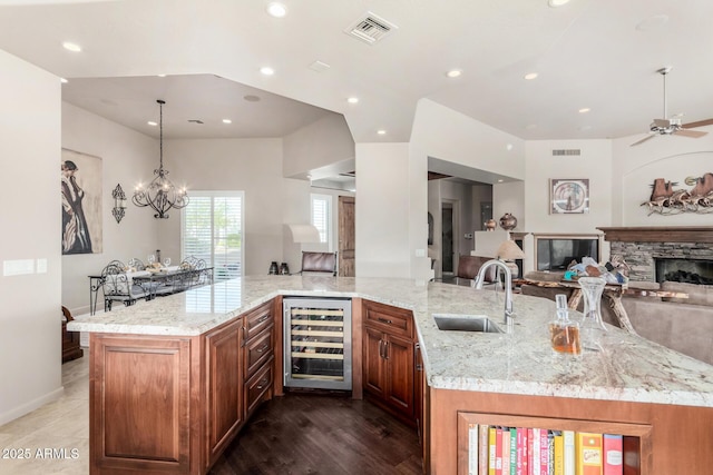 kitchen featuring wine cooler, sink, decorative light fixtures, a fireplace, and light stone countertops