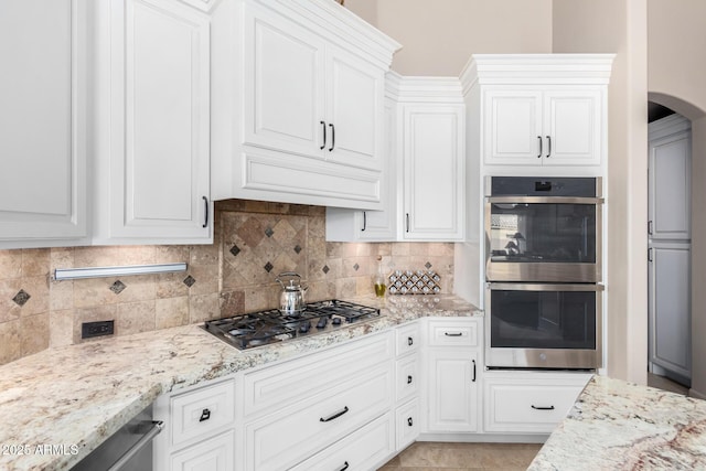 kitchen with white cabinetry, stainless steel appliances, light stone countertops, and backsplash