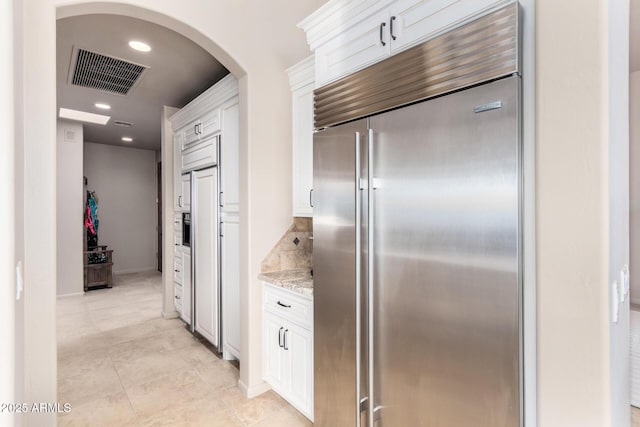 kitchen with white cabinetry, backsplash, light stone counters, and stainless steel built in refrigerator