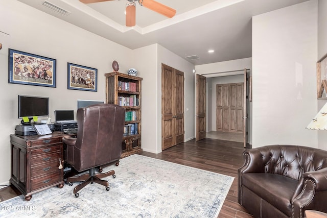 home office with dark hardwood / wood-style flooring, a raised ceiling, and ceiling fan