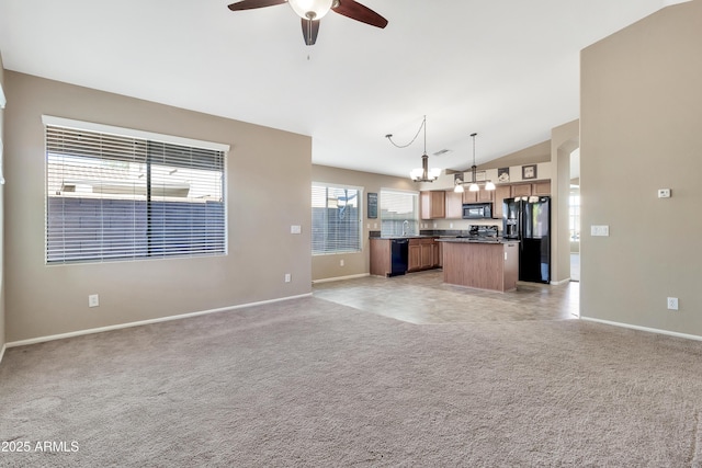 unfurnished living room featuring light carpet, ceiling fan with notable chandelier, and vaulted ceiling