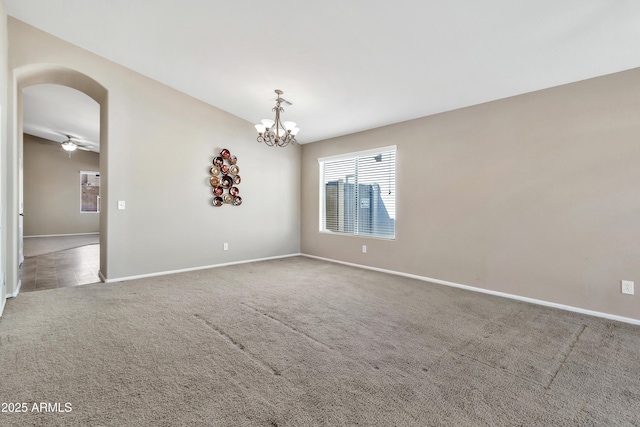 carpeted spare room featuring ceiling fan with notable chandelier