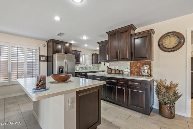 kitchen featuring decorative backsplash, stainless steel fridge, a center island, and dark brown cabinets