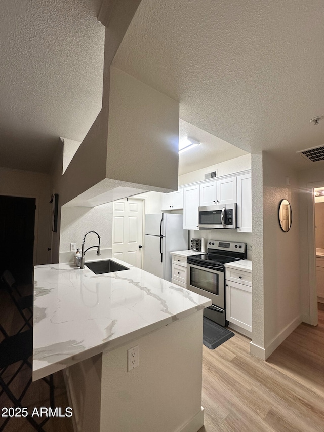 5345 E Van Buren St Unit 216, Phoenix, AZ 85008 - kitchen with stainless steel appliances, a textured ceiling, light wood-style floors, white cabinets, and light stone counters