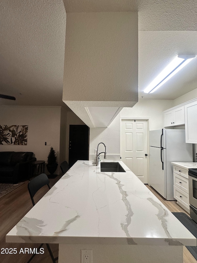 5345 E Van Buren St Unit 216, Phoenix, AZ 85008 - kitchen with a textured ceiling, freestanding refrigerator, white cabinetry, light wood-type flooring, and light stone countertops