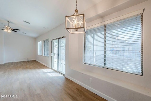 unfurnished dining area with visible vents, ceiling fan with notable chandelier, wood finished floors, baseboards, and lofted ceiling