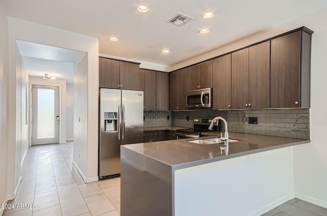 kitchen featuring sink, kitchen peninsula, decorative backsplash, dark brown cabinets, and appliances with stainless steel finishes