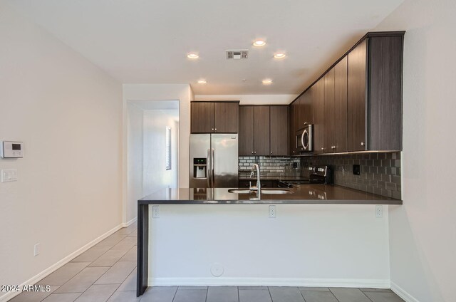 kitchen with kitchen peninsula, tasteful backsplash, dark brown cabinetry, stainless steel appliances, and sink