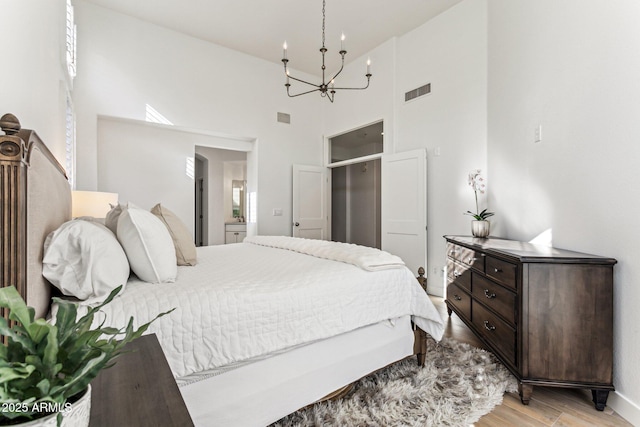 bedroom with a notable chandelier, light hardwood / wood-style floors, and a high ceiling