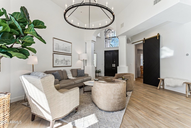 living room featuring ornate columns, an inviting chandelier, a towering ceiling, a barn door, and light hardwood / wood-style floors