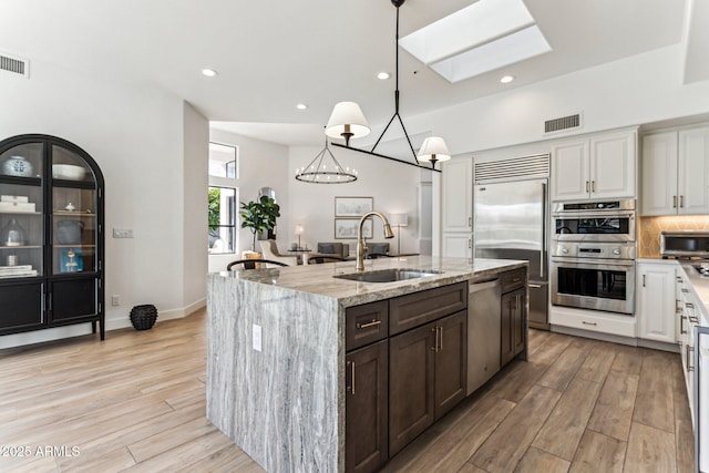 kitchen featuring appliances with stainless steel finishes, sink, a center island with sink, and white cabinets