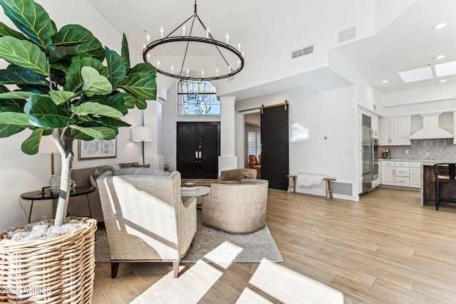 living room with a high ceiling, a barn door, a chandelier, and light wood-type flooring