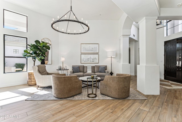 living room with ornate columns, light wood-type flooring, a high ceiling, and a notable chandelier