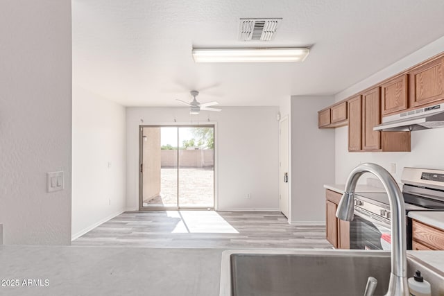 kitchen featuring ceiling fan, brown cabinetry, visible vents, a sink, and under cabinet range hood