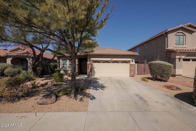 view of front of property featuring a garage, a tile roof, fence, stone siding, and driveway