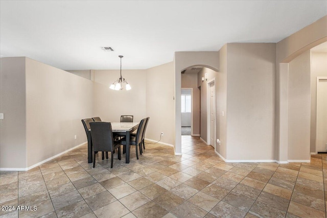 dining room featuring arched walkways, visible vents, stone finish floor, a chandelier, and baseboards