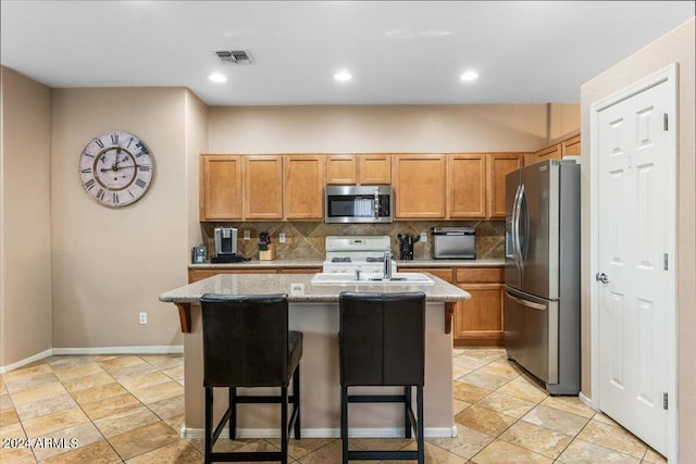 kitchen with stainless steel appliances, visible vents, a center island with sink, and a kitchen breakfast bar