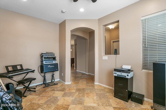 office area featuring baseboards, arched walkways, a ceiling fan, and stone finish flooring