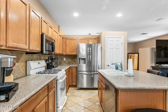 kitchen with light stone counters, stainless steel appliances, a sink, decorative backsplash, and an island with sink