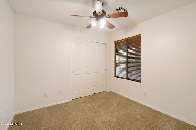 unfurnished bedroom with a closet, light colored carpet, and ceiling fan