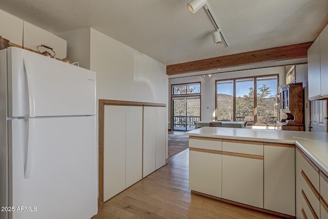 kitchen featuring rail lighting, white cabinetry, white refrigerator, light hardwood / wood-style floors, and a textured ceiling