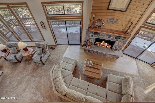 living room with a high ceiling, a stone fireplace, and light hardwood / wood-style flooring