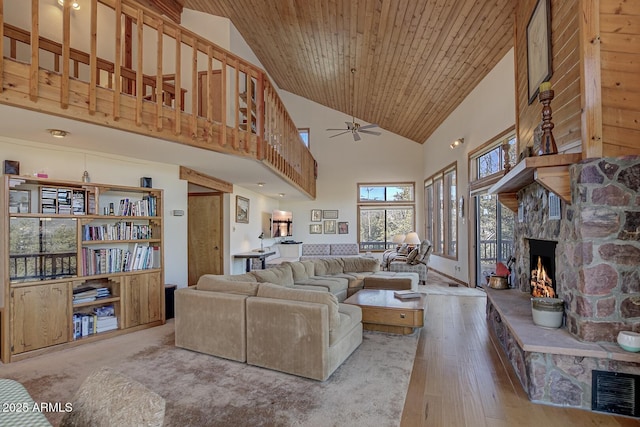 living room featuring ceiling fan, hardwood / wood-style floors, high vaulted ceiling, a stone fireplace, and wooden ceiling